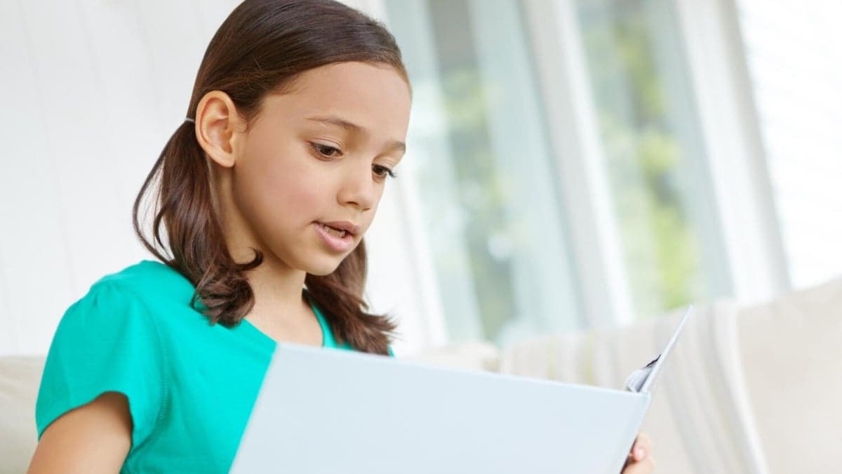 Child reading a physical book on a sofa